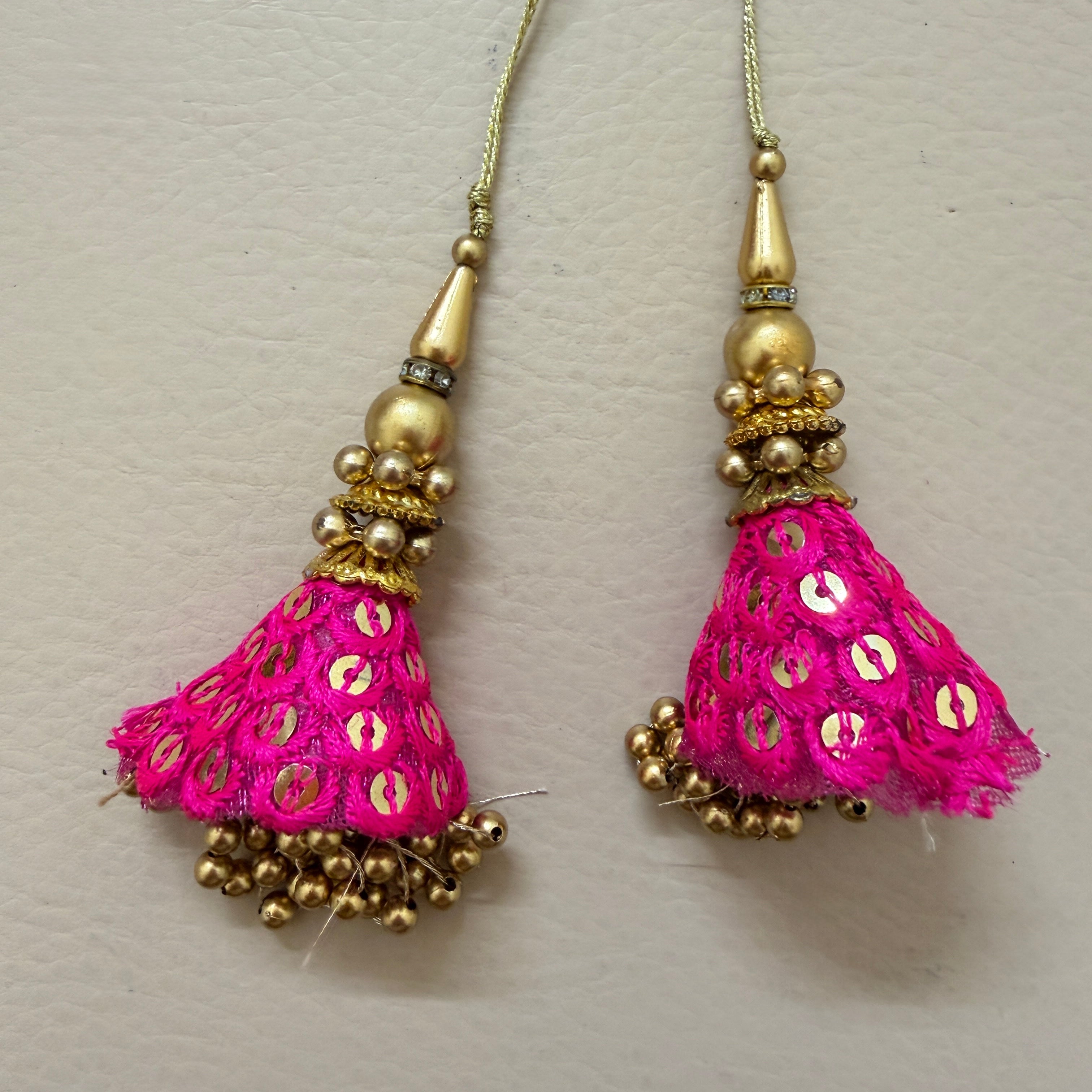 Pair of pink tassel earrings with gold accents on a light gray background