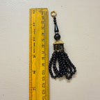 Black beaded tassel with gold accent next to a ruler on a light gray background