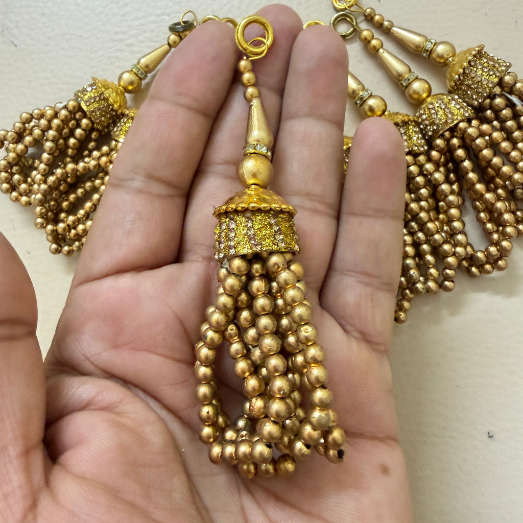 Gold beaded tassel held between fingers against a neutral background