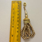 Gold tassel charm next to a ruler on a light gray background