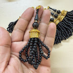 Black beaded necklace with gold accents held in a hand against a neutral background