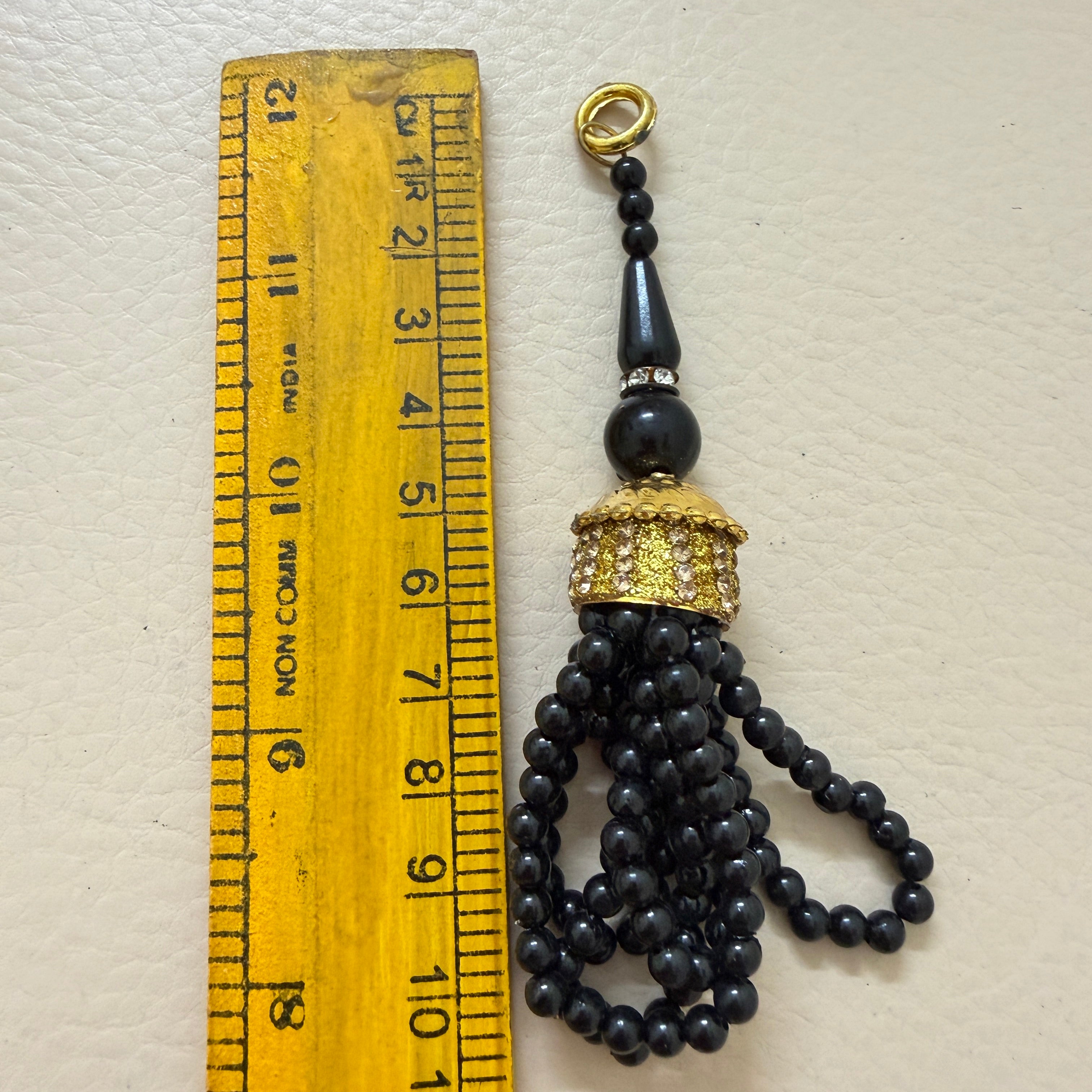 Black beaded tassel with gold cap next to a ruler on a white background
