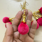 Decorative keychain with pink tassels and gold accents held in a hand against a light background