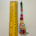 Colorful beaded ornament with a gold top section next to a wooden ruler for scale on a white background.