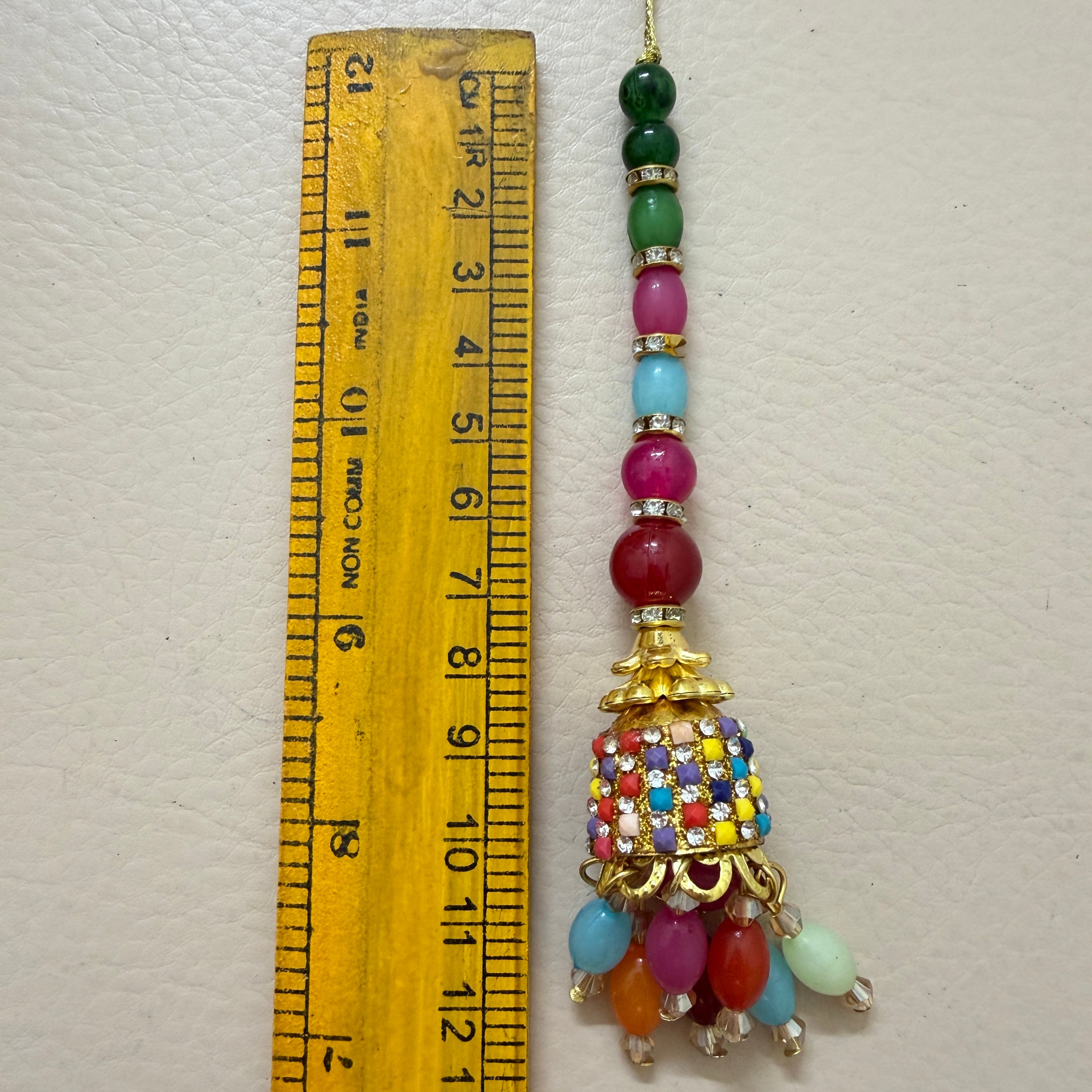 Colorful beaded ornament with a gold top section next to a wooden ruler for scale on a white background.