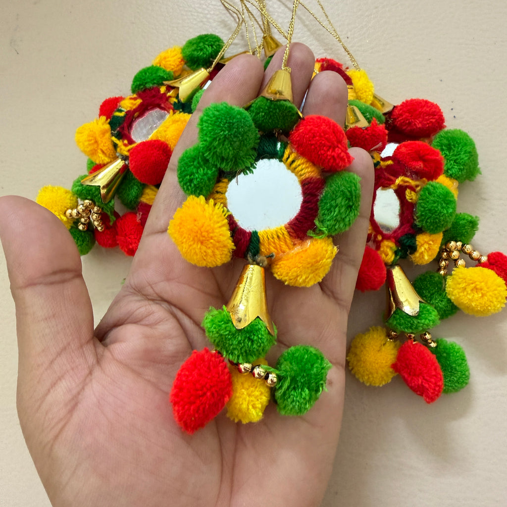 Colorful pom-pom earrings held in a hand with a plain background