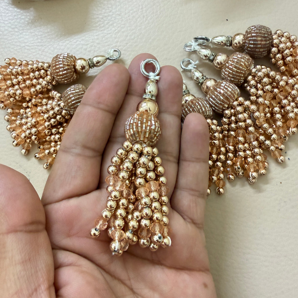 Gold beaded tassel held between fingers with a blurred background