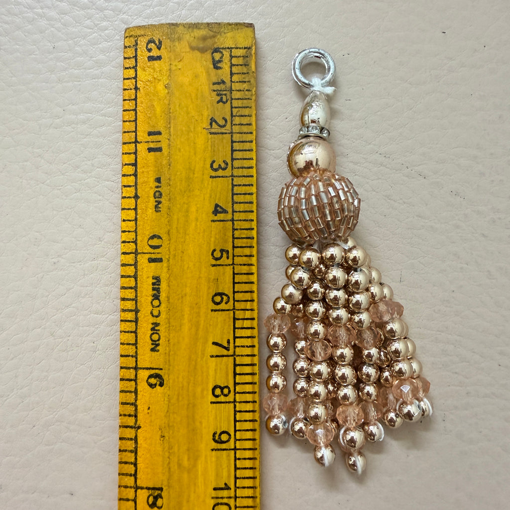 Gold beaded tassel with a silver clasp next to a ruler on a light gray background