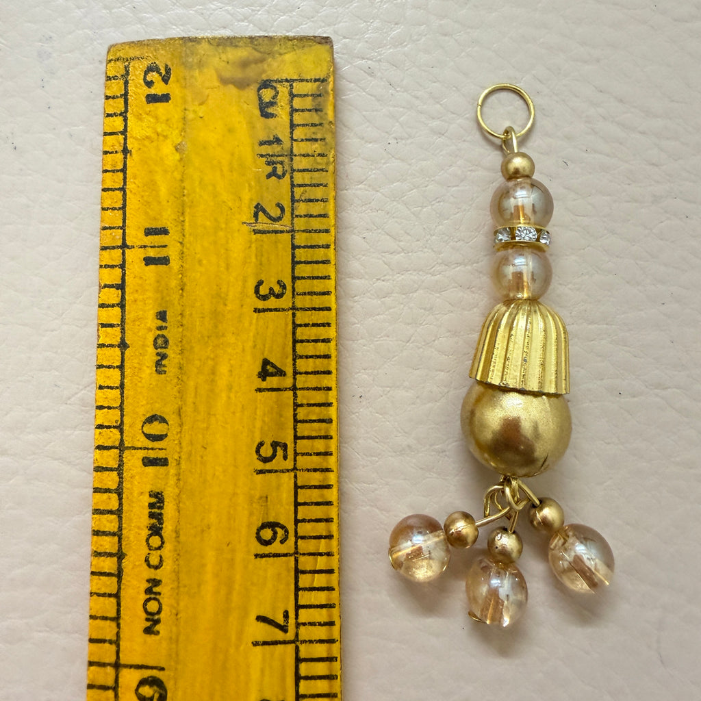 Gold and pearl decorative charm next to a ruler for scale on a light gray background