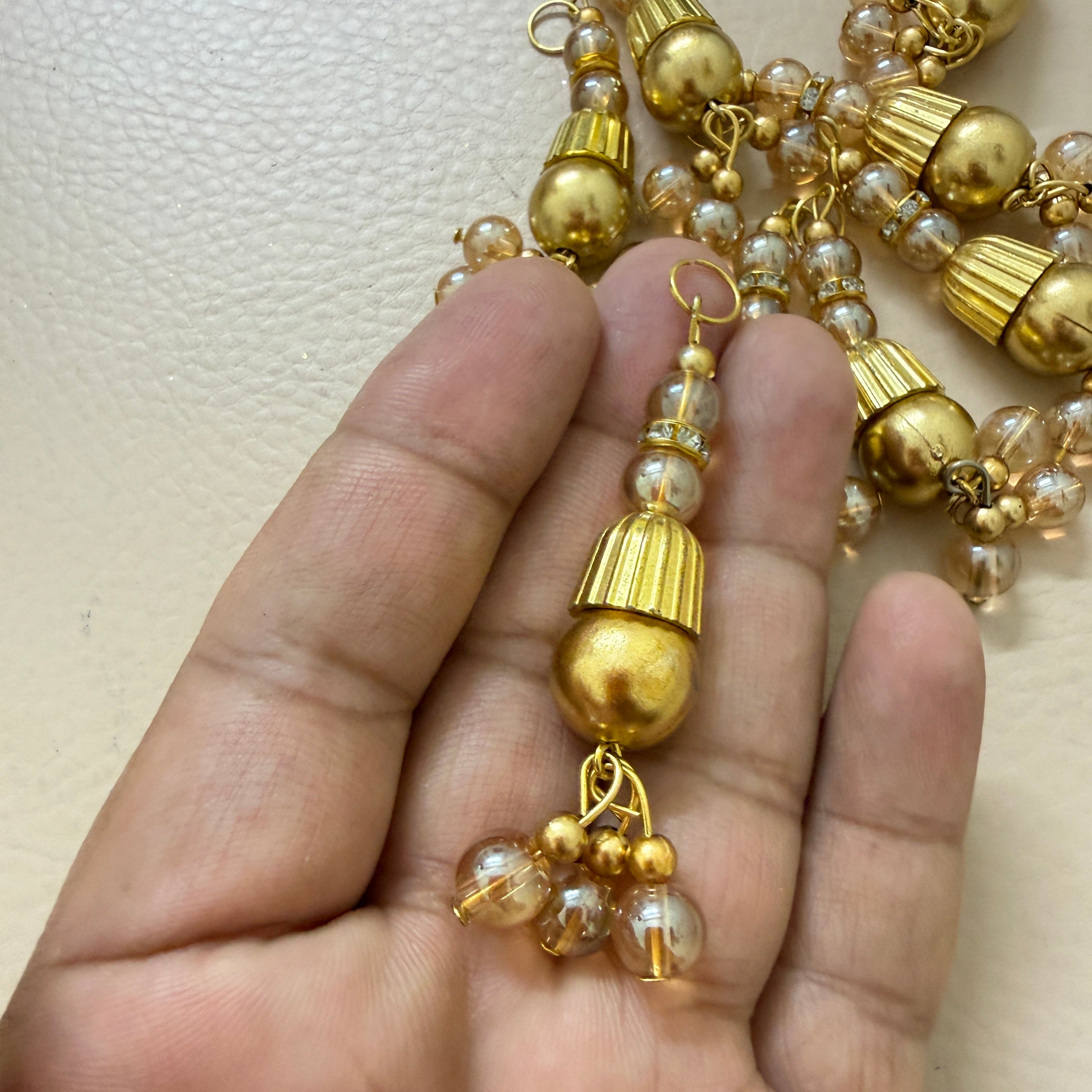 Gold and pearl beaded necklace held by a hand on a light background