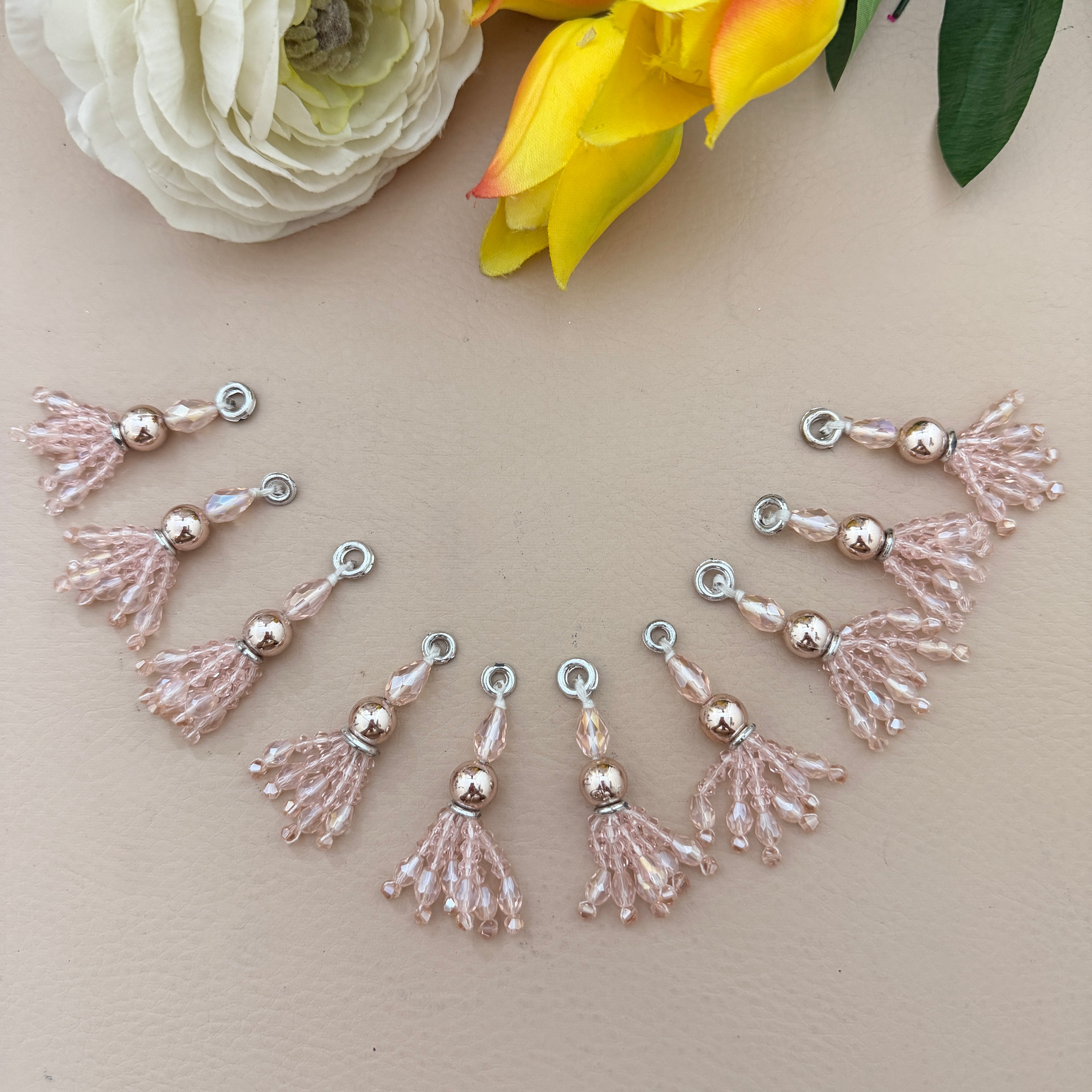 Decorative tassel charms on a beige surface with flowers in the background