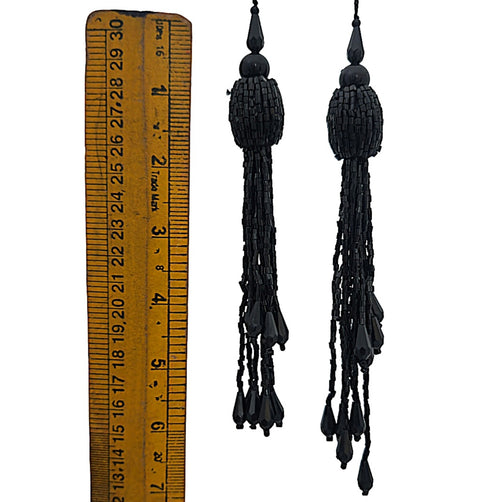 Black tassel earrings with a ruler for scale on a white background