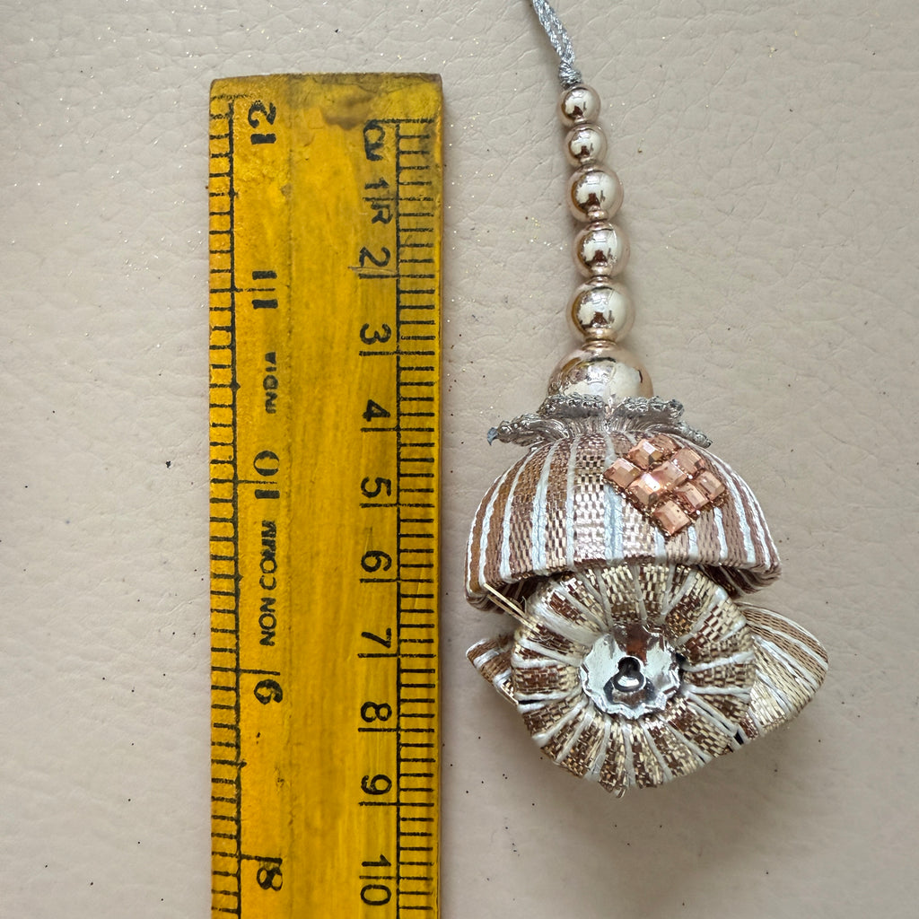 Decorative shell pendant with beads next to a ruler for scale on a beige background