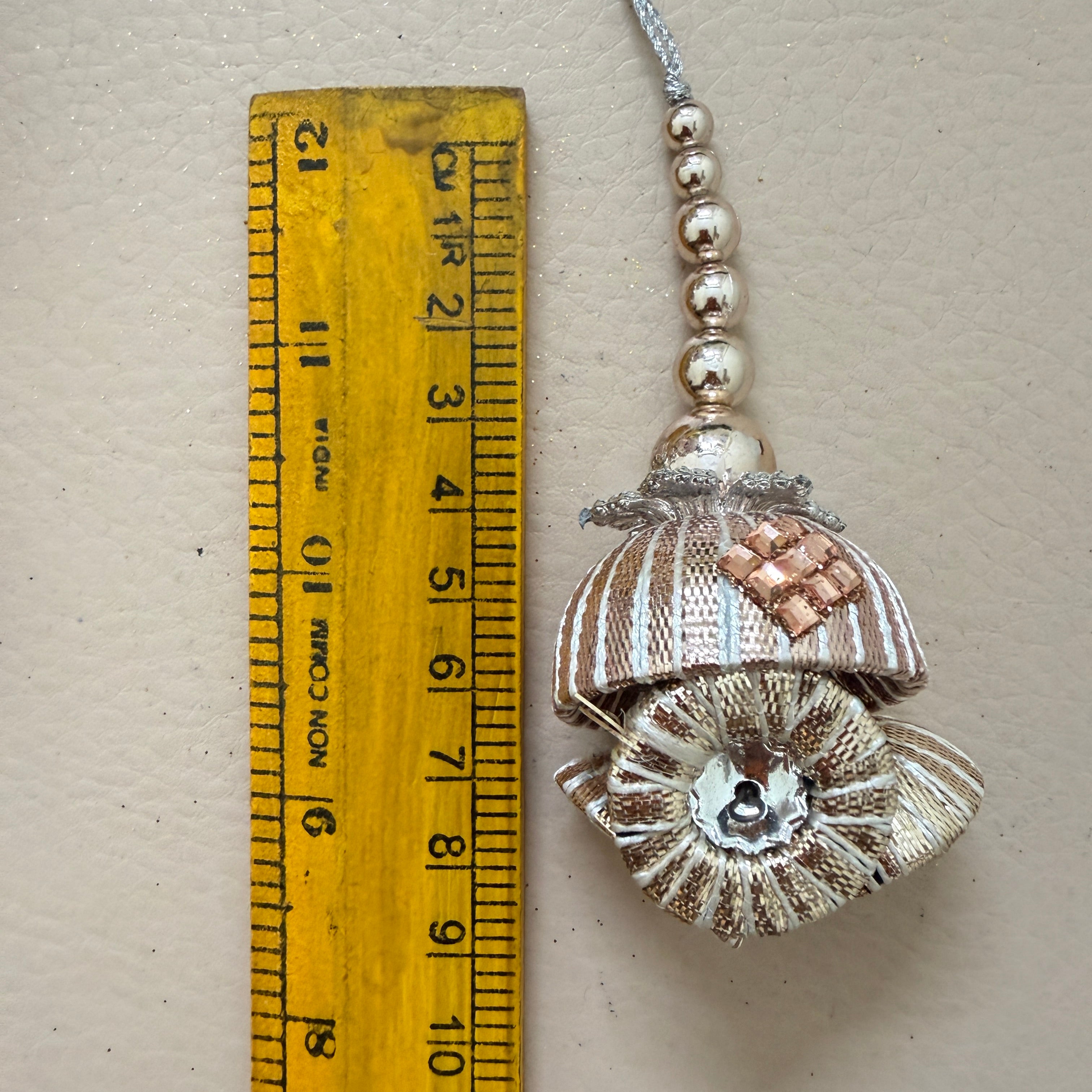 Decorative shell pendant with beads next to a ruler for scale on a beige background