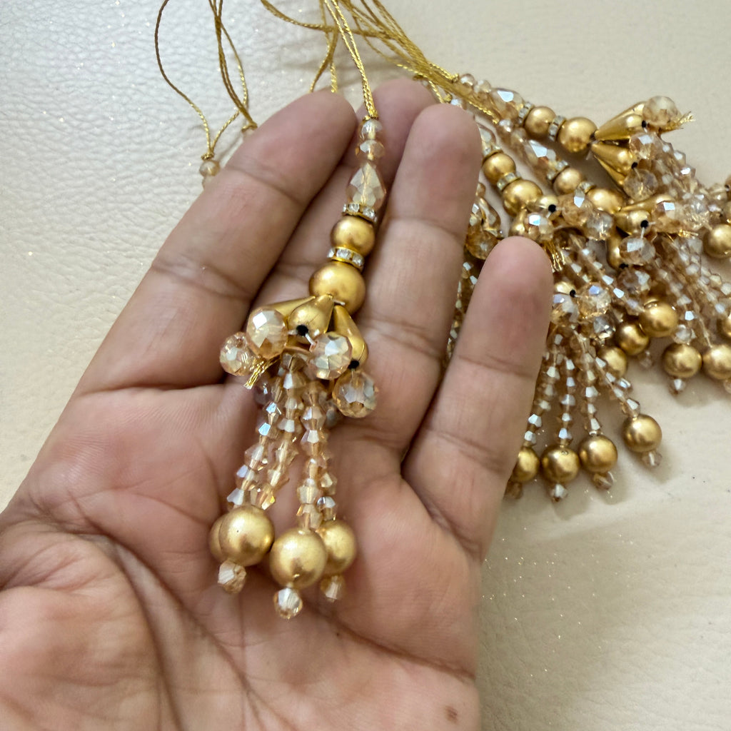Gold beaded necklace held by a hand against a neutral background