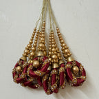 Decorative hanging ornaments with gold beads and maroon fabric on a light gray background