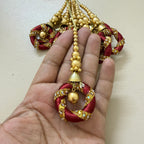 Decorative red and gold pendant held in a hand against a plain background
