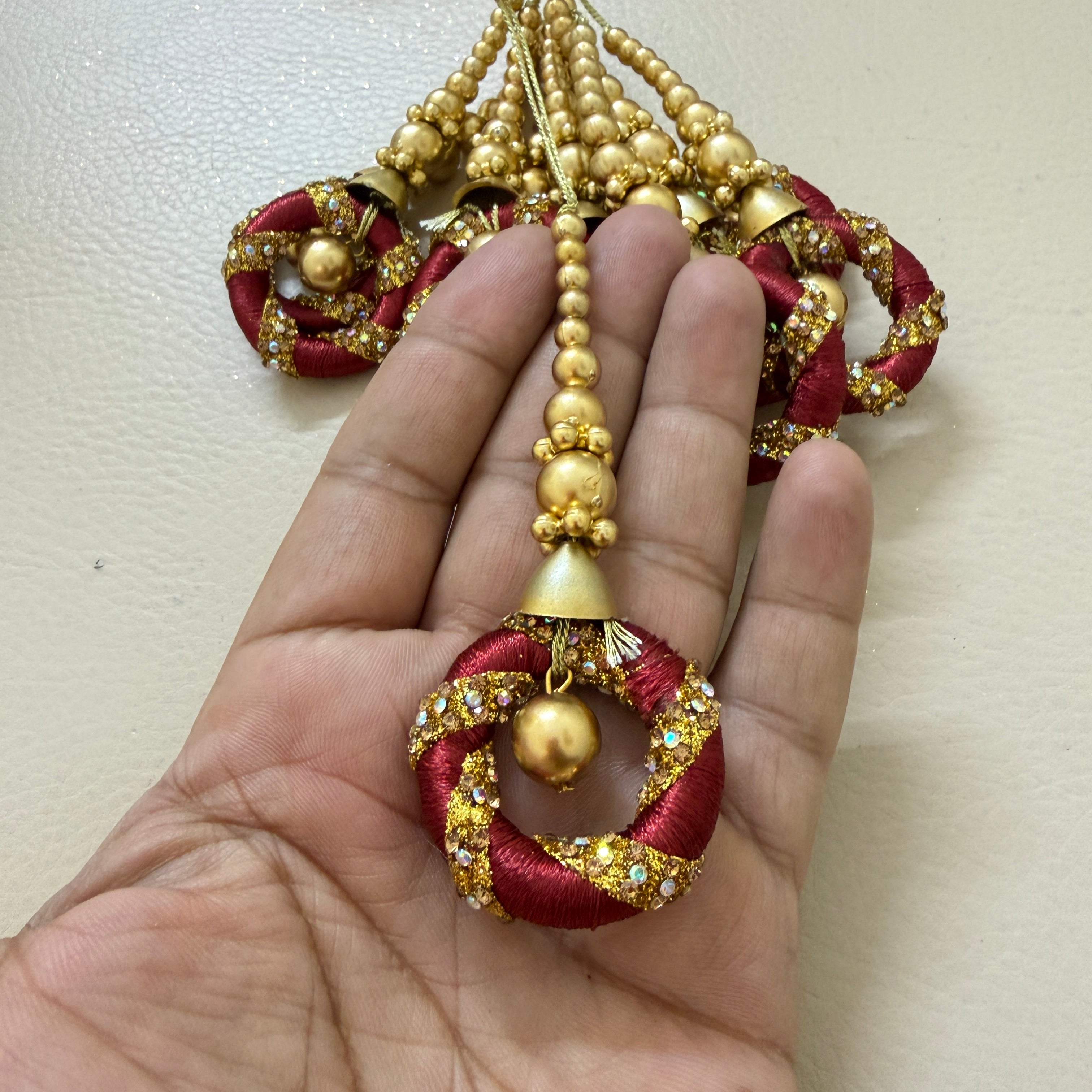 Decorative red and gold pendant held in a hand against a plain background