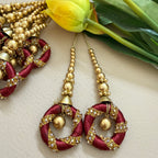 Decorative earrings with gold and red details on a light background with flowers.