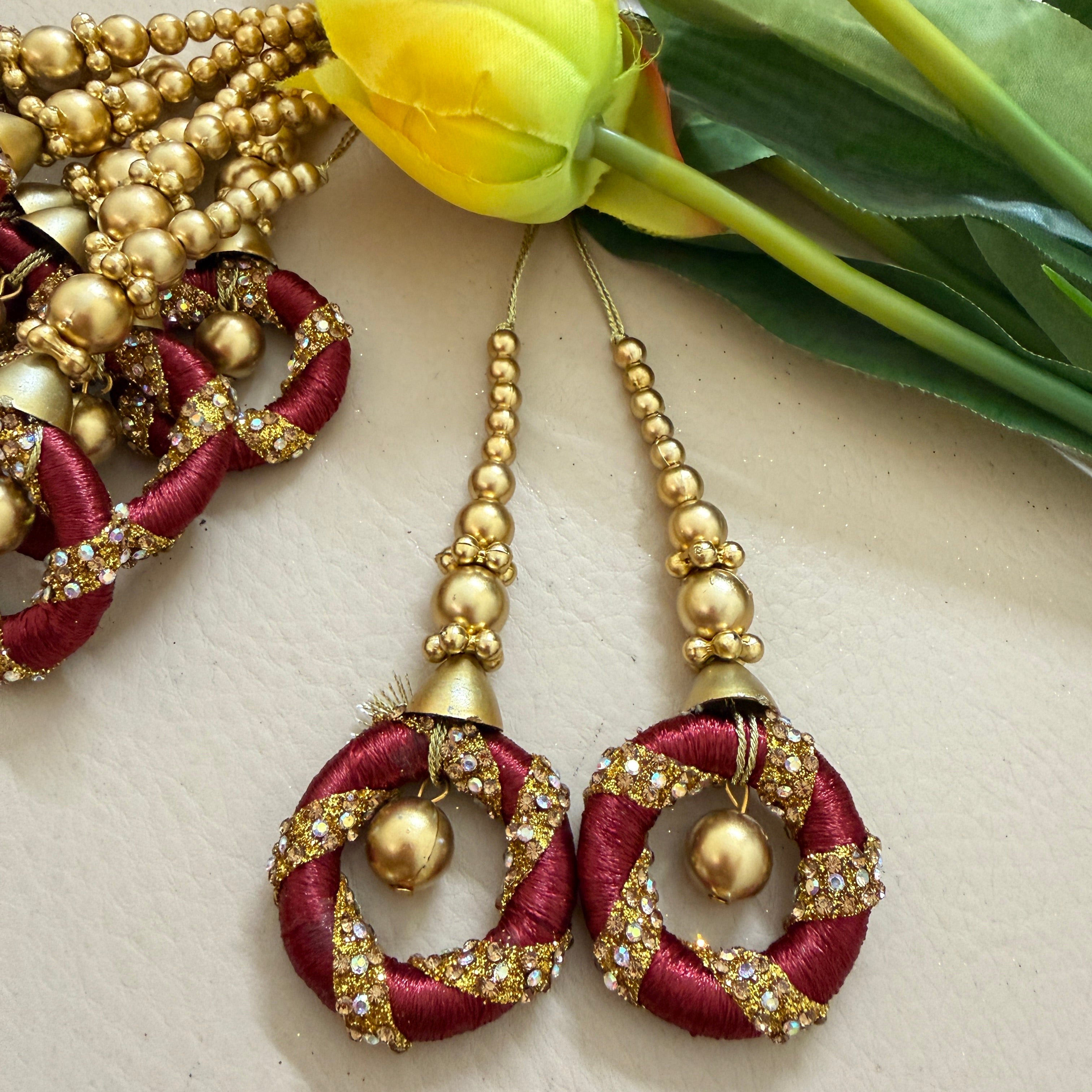 Decorative earrings with gold and red details on a light background with flowers.