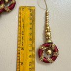 Decorative red and gold pendant with a ruler for scale on a light background