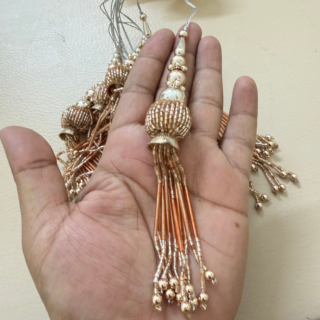 Gold beaded tassel held in a hand against a light background
