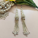 Silver tassel earrings on a light pink surface with green leaves in the background