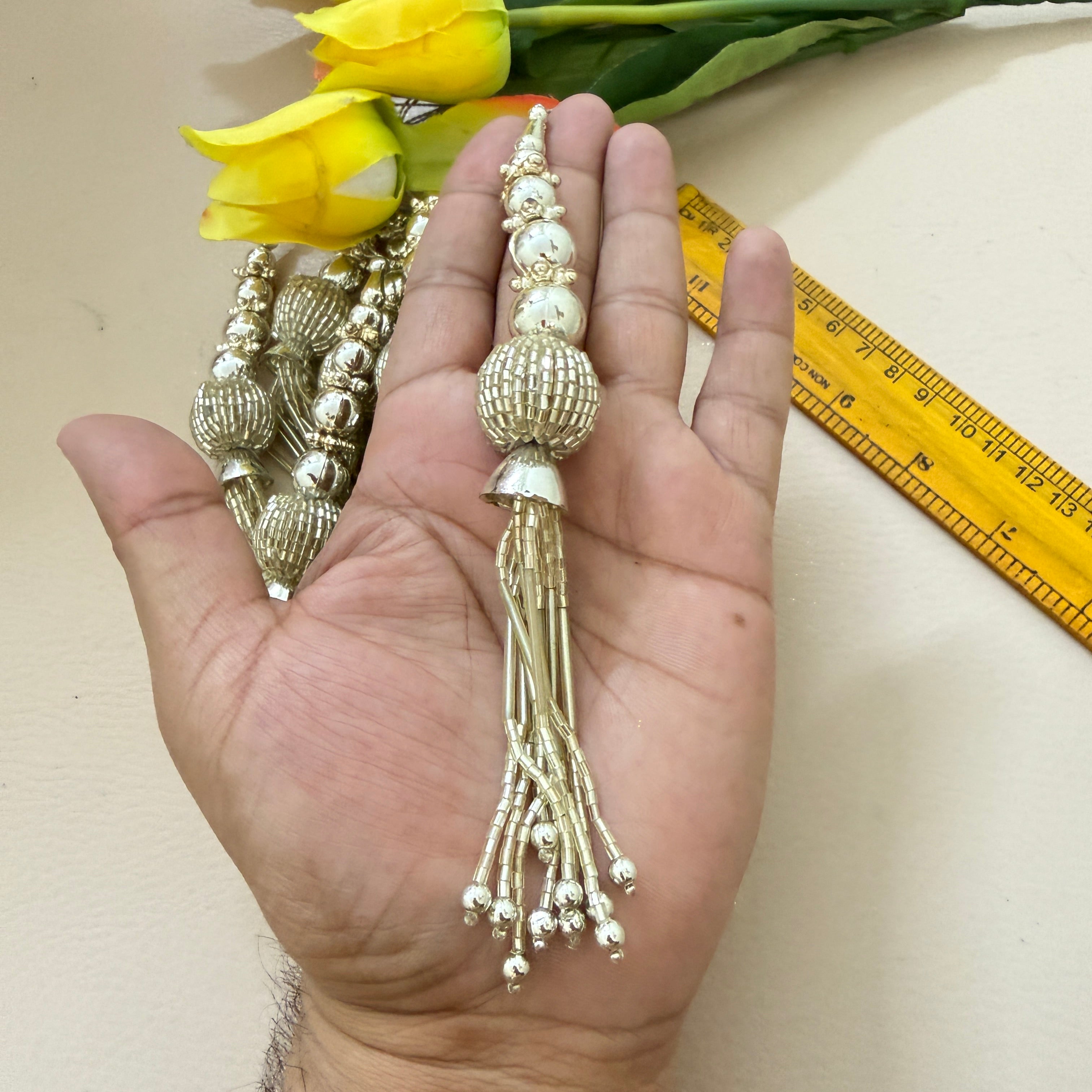 Decorative gold string held in a hand with yellow tulips and a ruler in the background