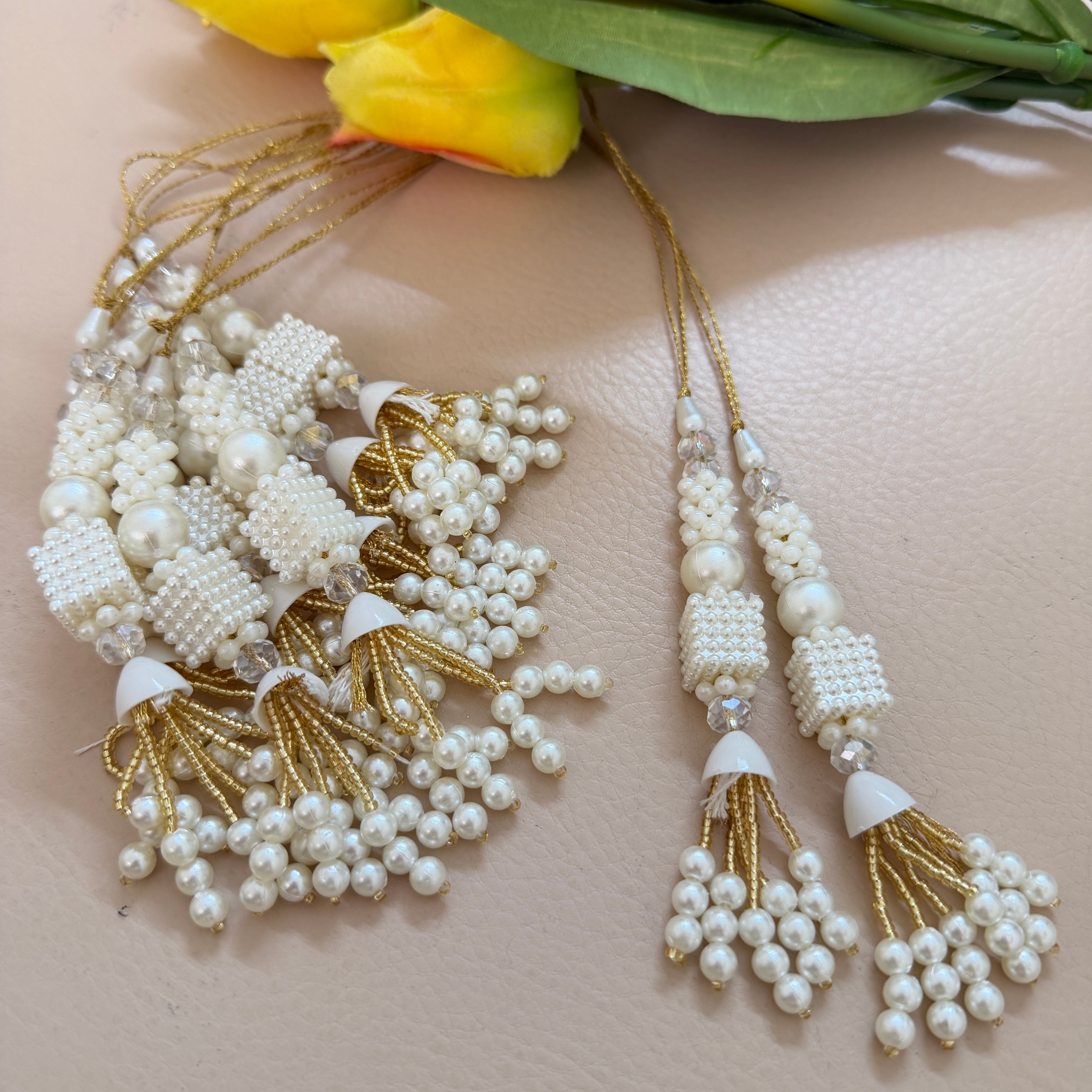 Pearl and gold tassel necklace on a light pink background with yellow flowers.
