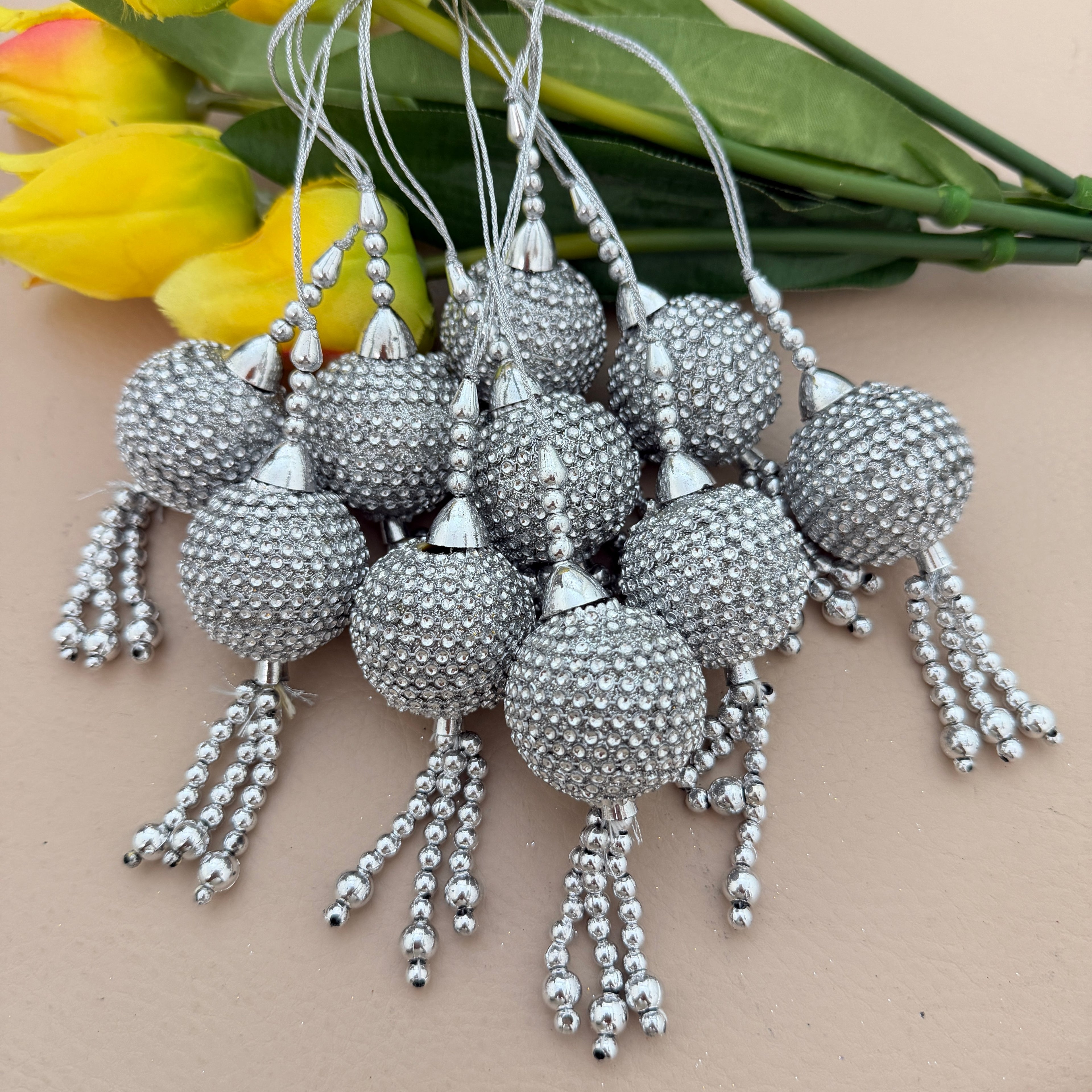 Silver beaded tassels with a beige background and yellow flowers.