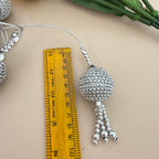 Silver beaded ornament with tassels next to a ruler on a beige surface