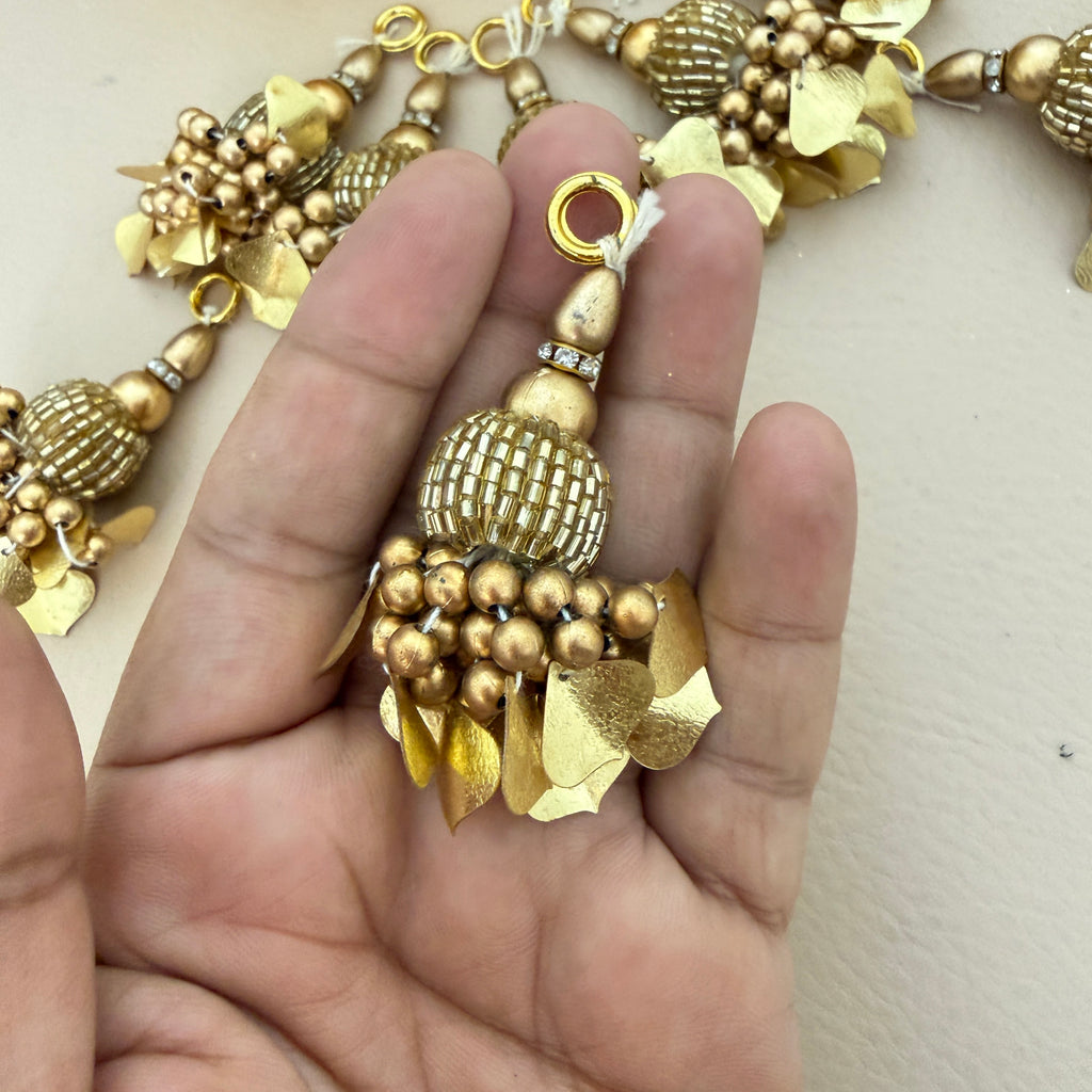 Gold necklace with intricate design held by a hand against a neutral background