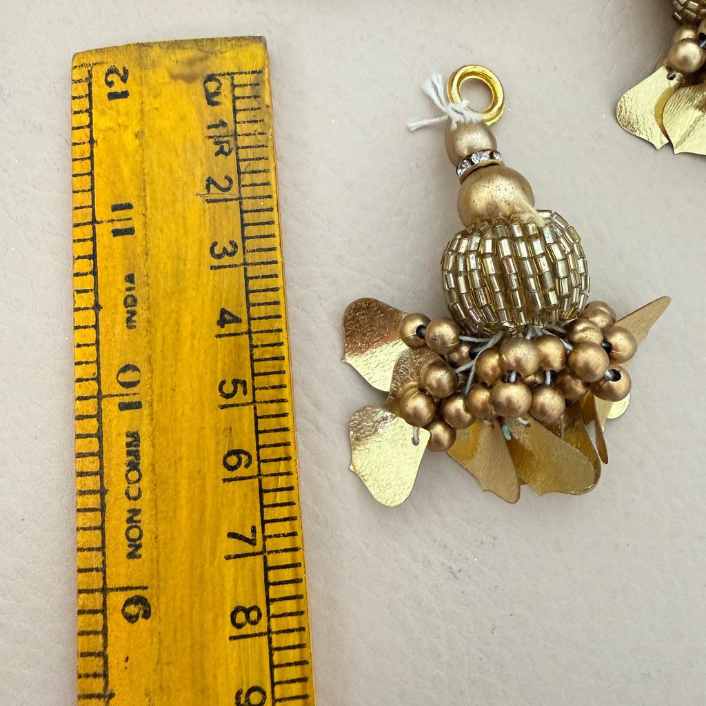 Gold decorative pendant next to a wooden ruler for scale