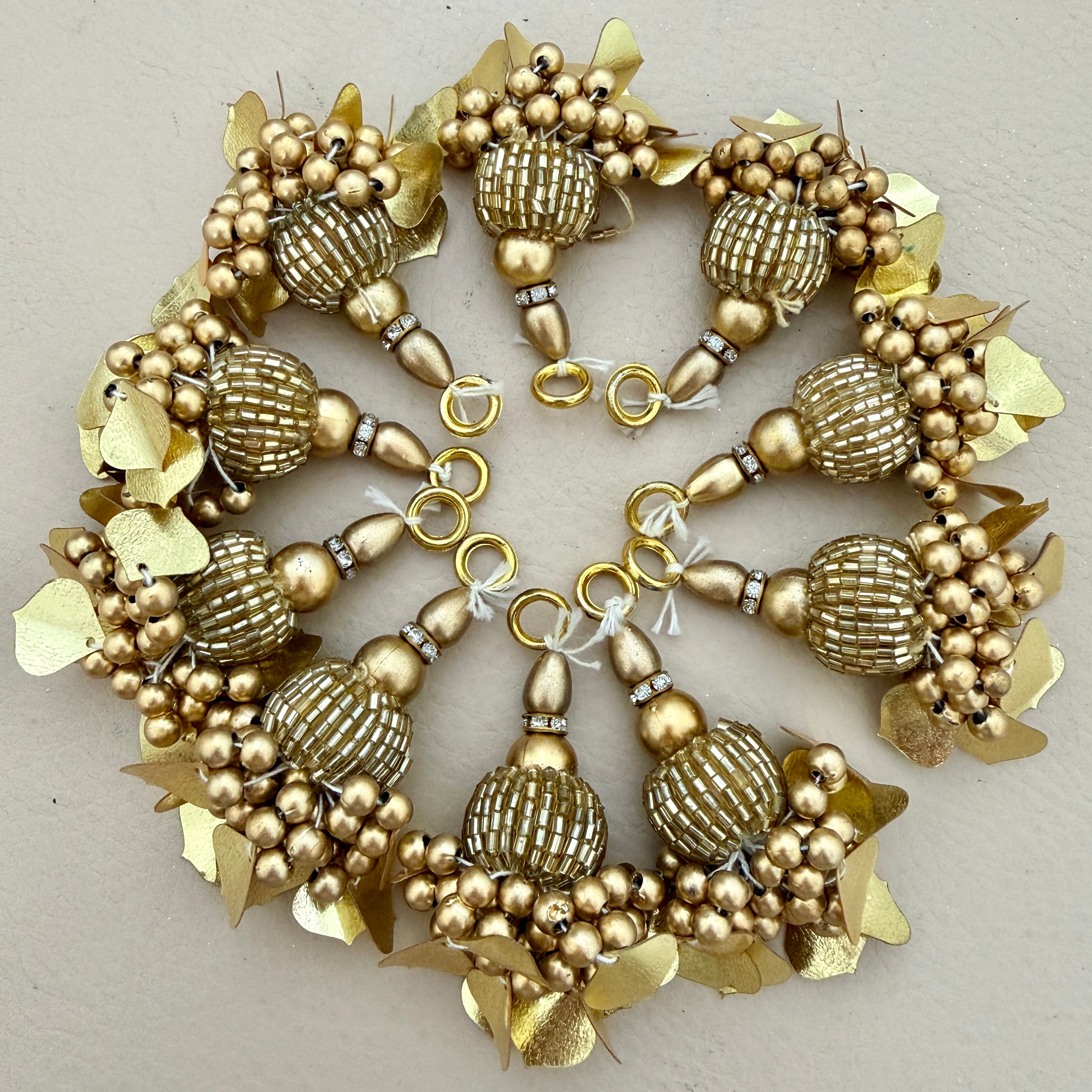 Decorative gold wreath with spherical beads and leaf-like elements on a light gray background