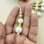 Pearl and gold beaded charm held between fingers with a blurred background