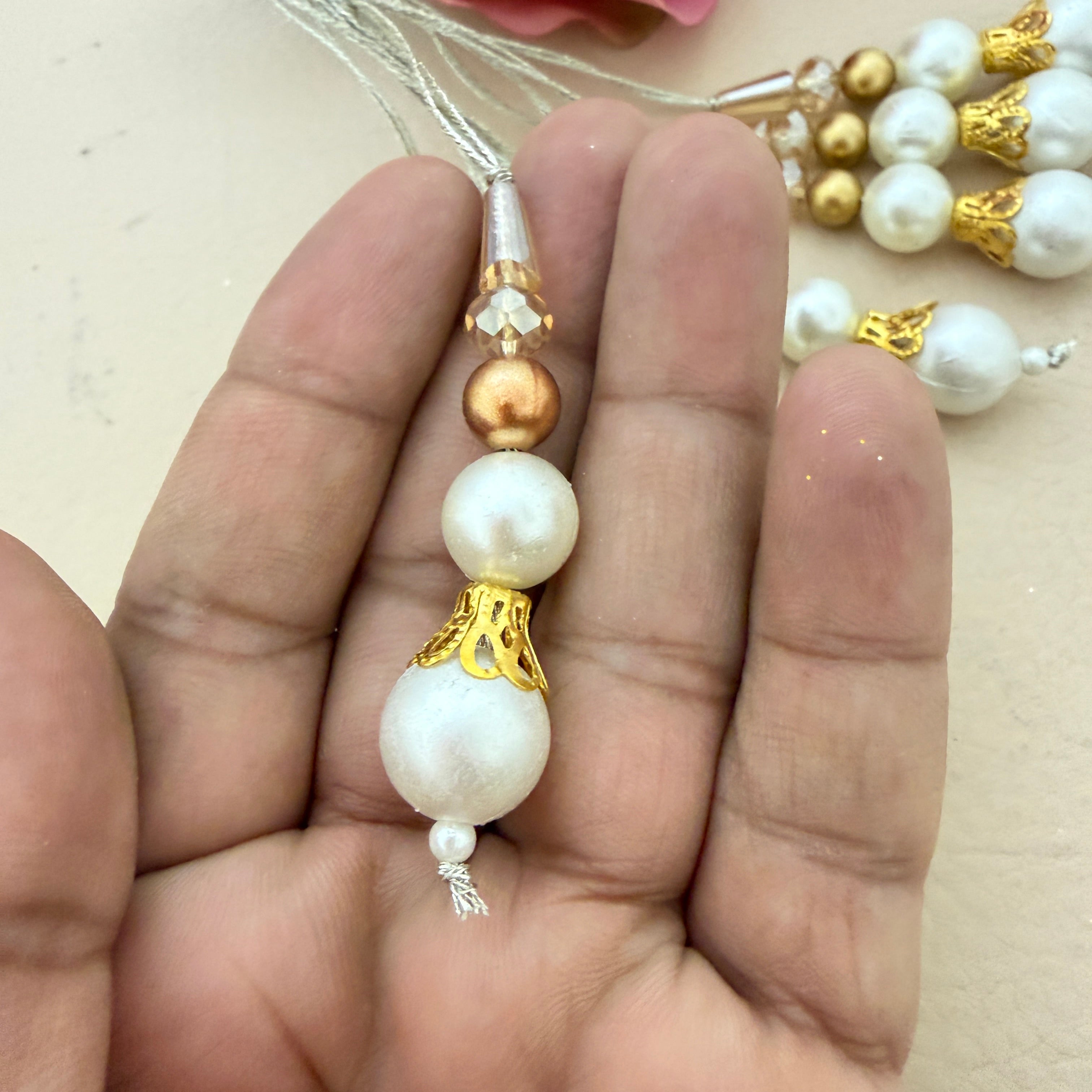Pearl and gold beaded charm held between fingers with a blurred background