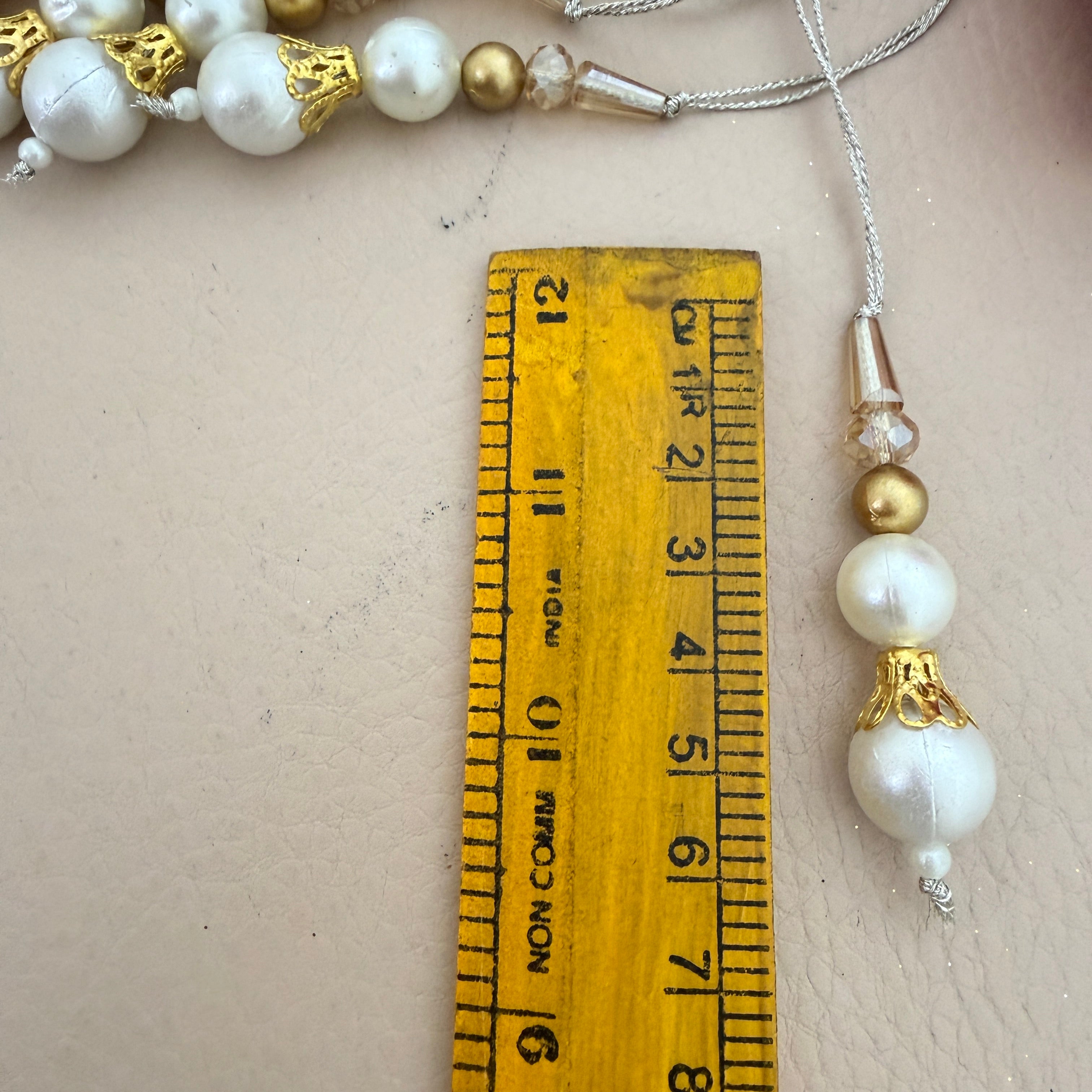 Pearl and gold beaded necklace next to a ruler on a neutral background