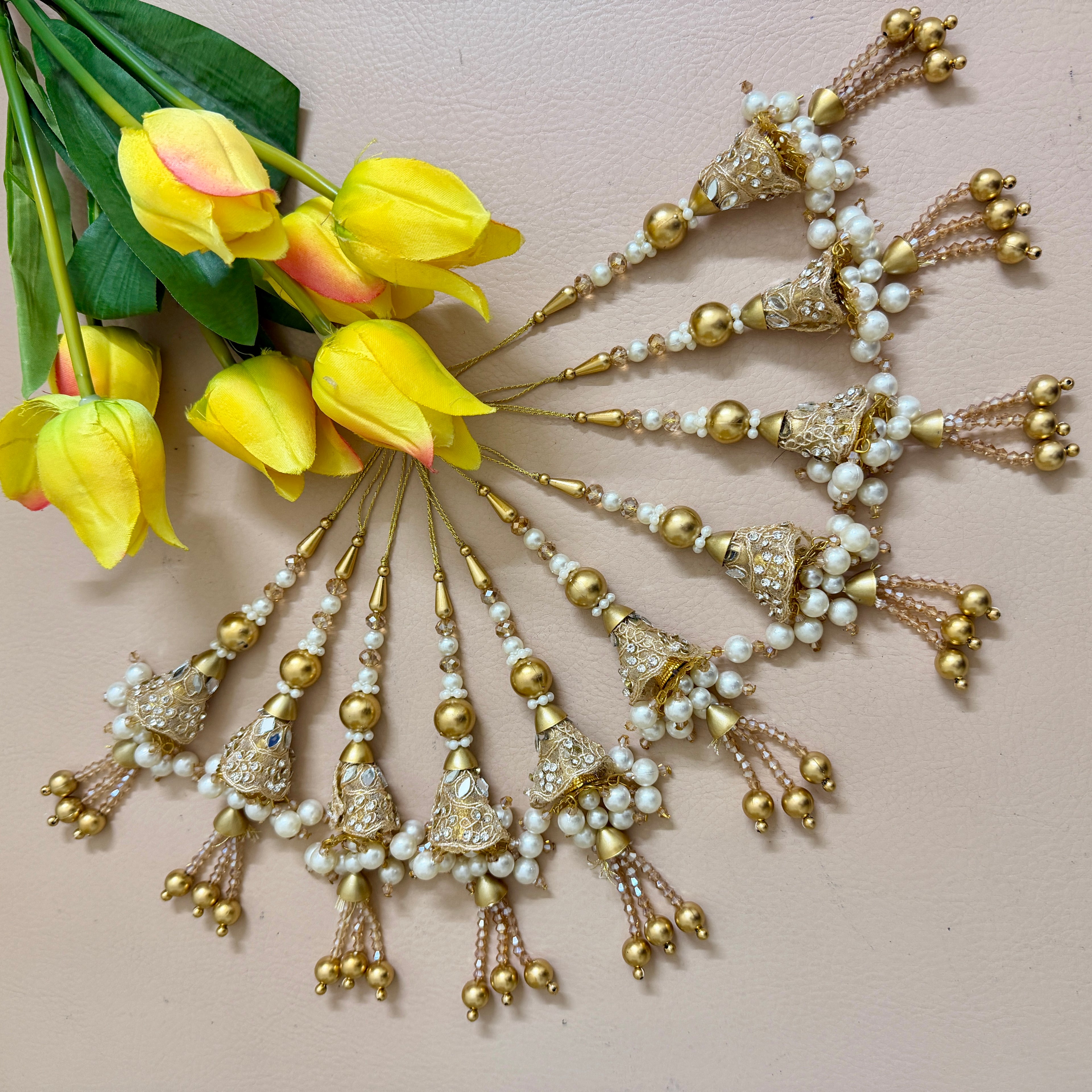Decorative hair accessories with pearls and gold elements next to yellow tulips on a light pink background