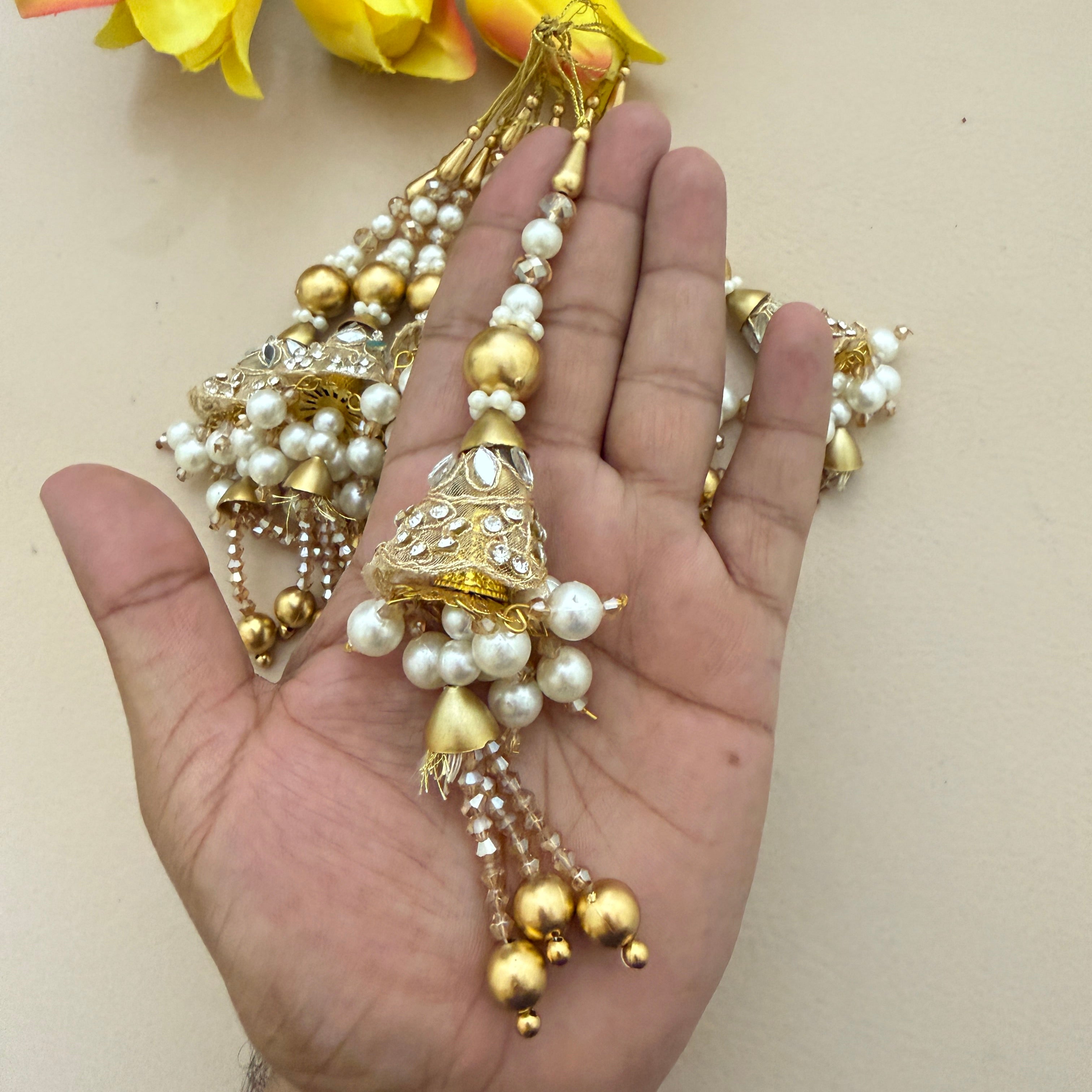 Gold and pearl jewelry piece held in a hand with a light background