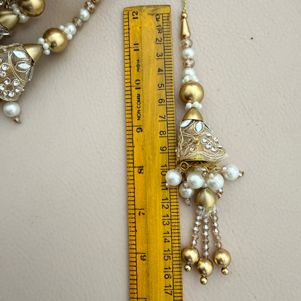 Decorative gold and pearl tassel with a ruler for scale on a light background