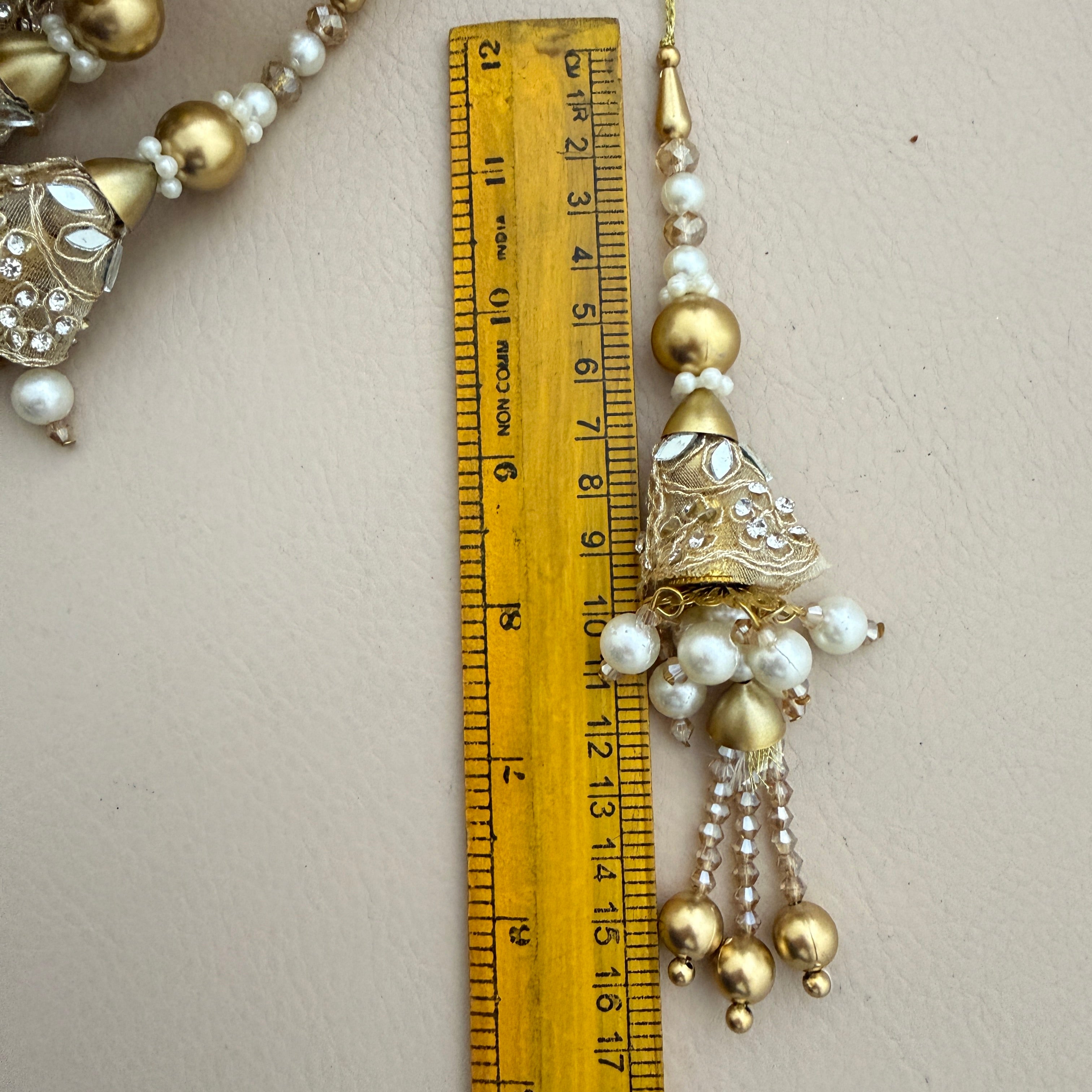 Decorative gold and pearl tassel with a ruler for scale on a light background