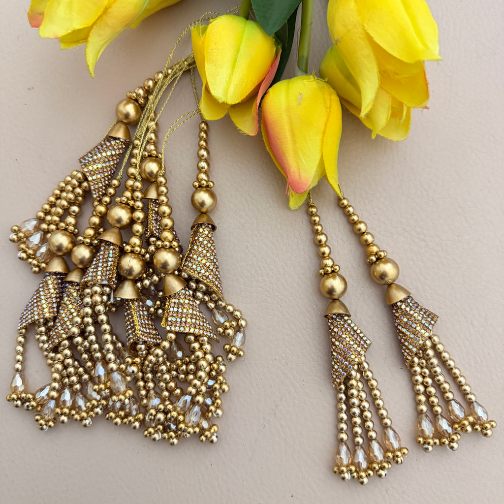 Gold beaded earrings with tassels on a light background with yellow flowers.