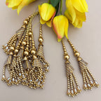 Gold beaded earrings with tassels on a light background with yellow flowers.