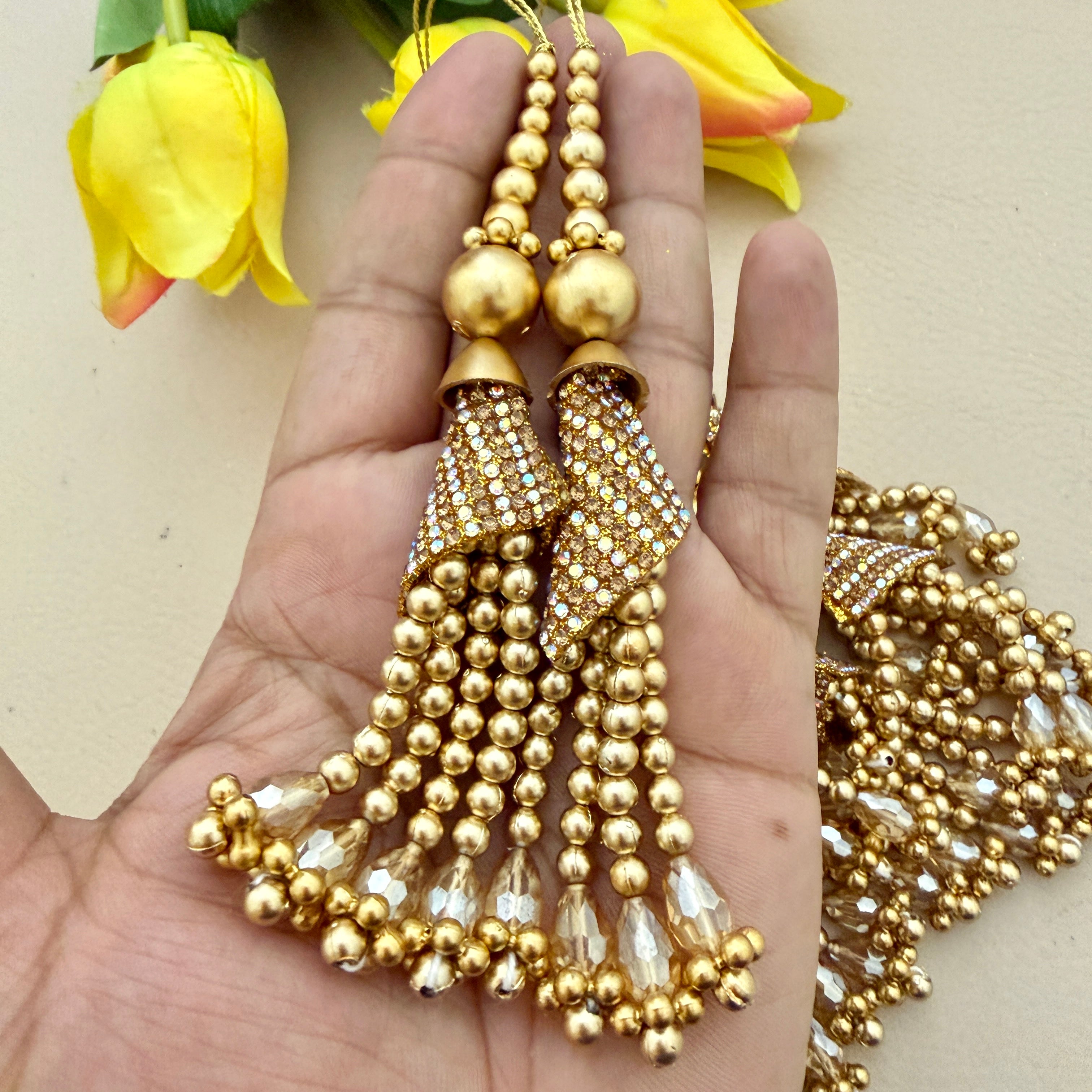 Gold beaded tassel earrings held in a hand with yellow tulips in the background