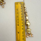 Gold necklace with beads and a ruler for scale on a light gray background