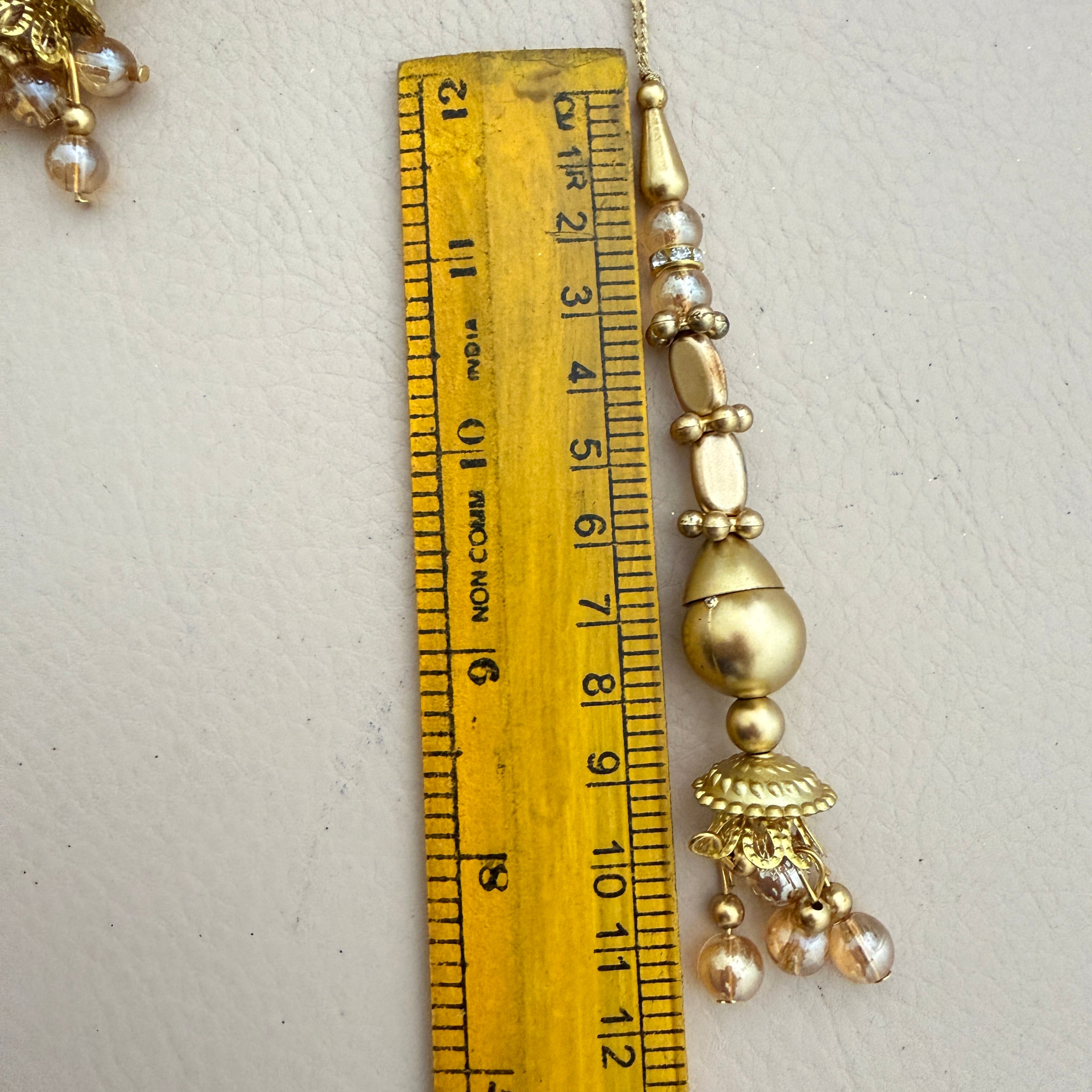 Gold necklace with beads and a ruler for scale on a light gray background