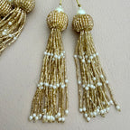 Gold beaded tassel earrings with pearls on a beige background