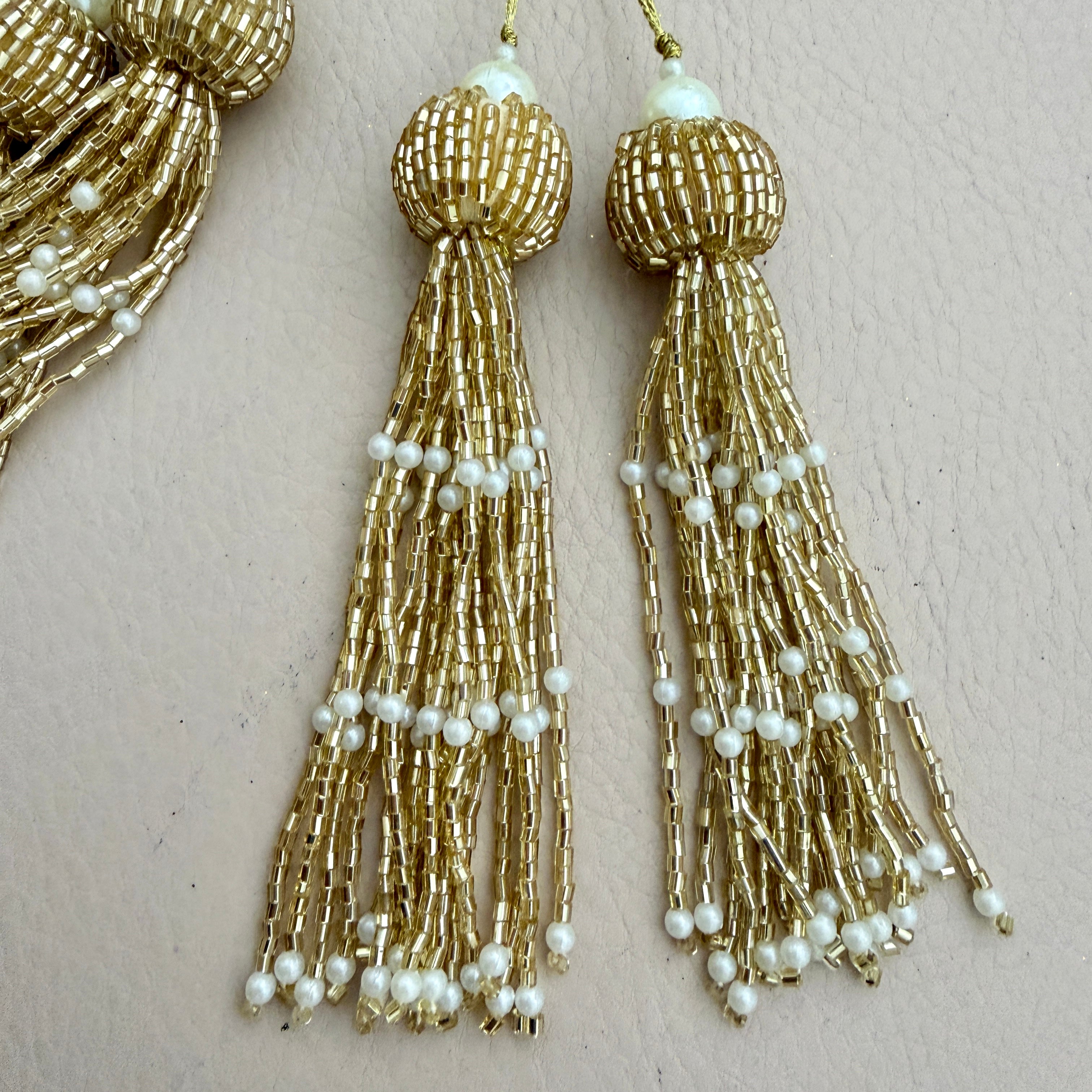 Gold beaded tassel earrings with pearls on a beige background