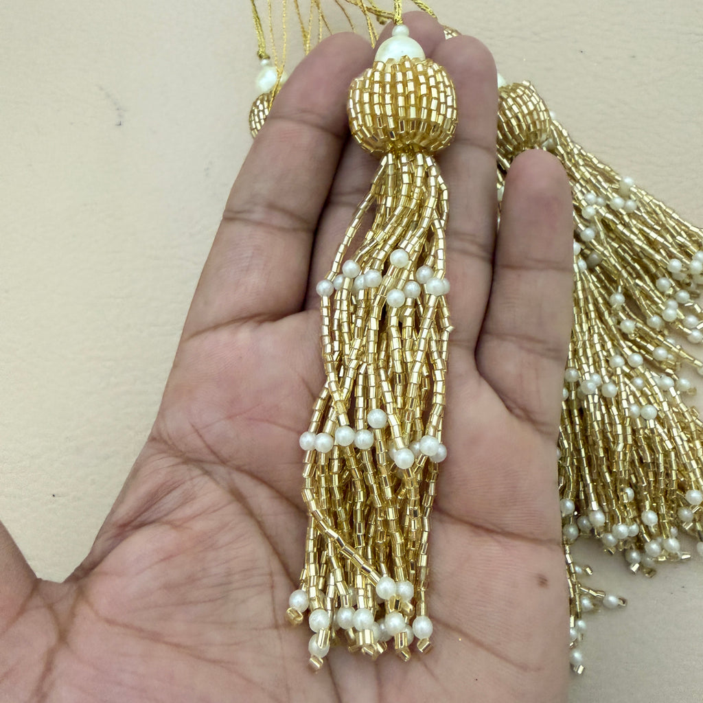 Gold tassel with pearls held in a hand against a beige background