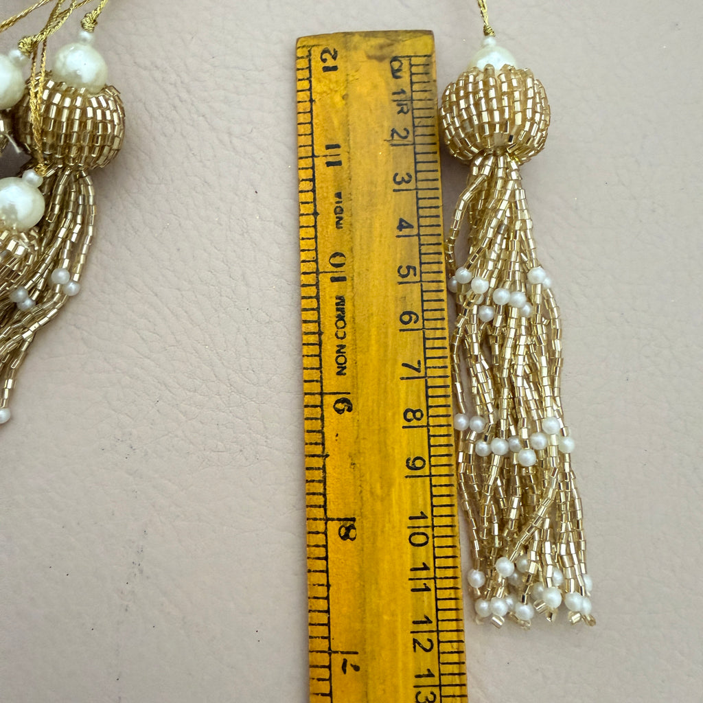 Gold tassel earrings with pearls next to a wooden ruler on a beige background